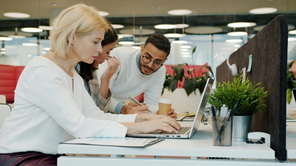 colleagues men and women using laptops and talking in shared workspace office.